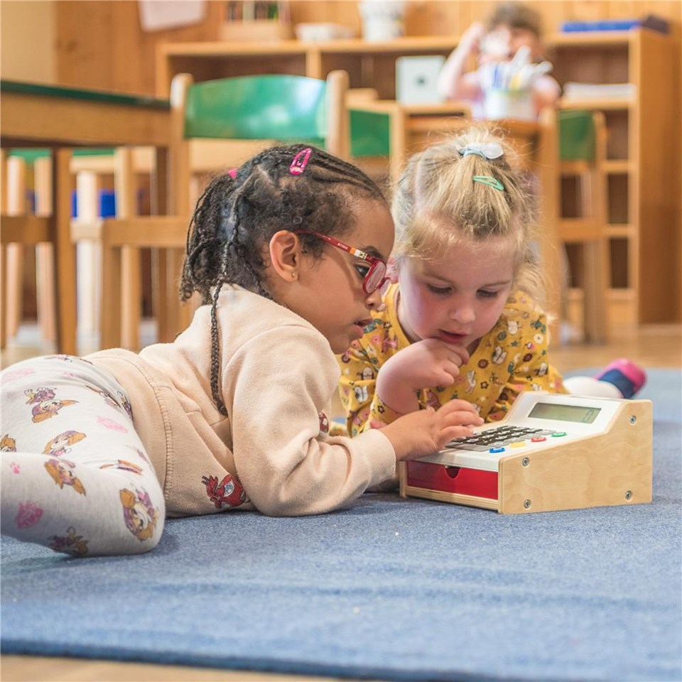  Zwei kleine Mädchen spielen auf dem Boden mit einem Spielzeug.