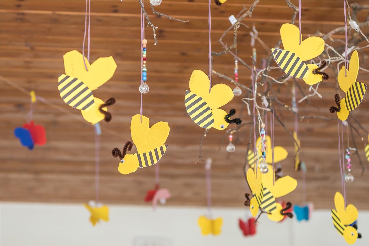 Hängende Dekoration aus Papierbienen und -schmetterlingen in verschiedenen Farben, die fröhlich im Raum schwingen.
