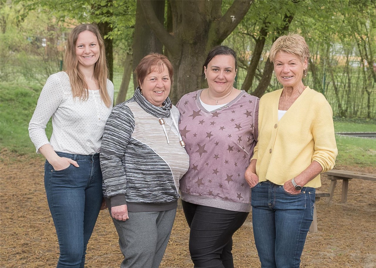 Vier Frauen stehen nebeneinander vor einem Baum und lächeln in die Kamera.