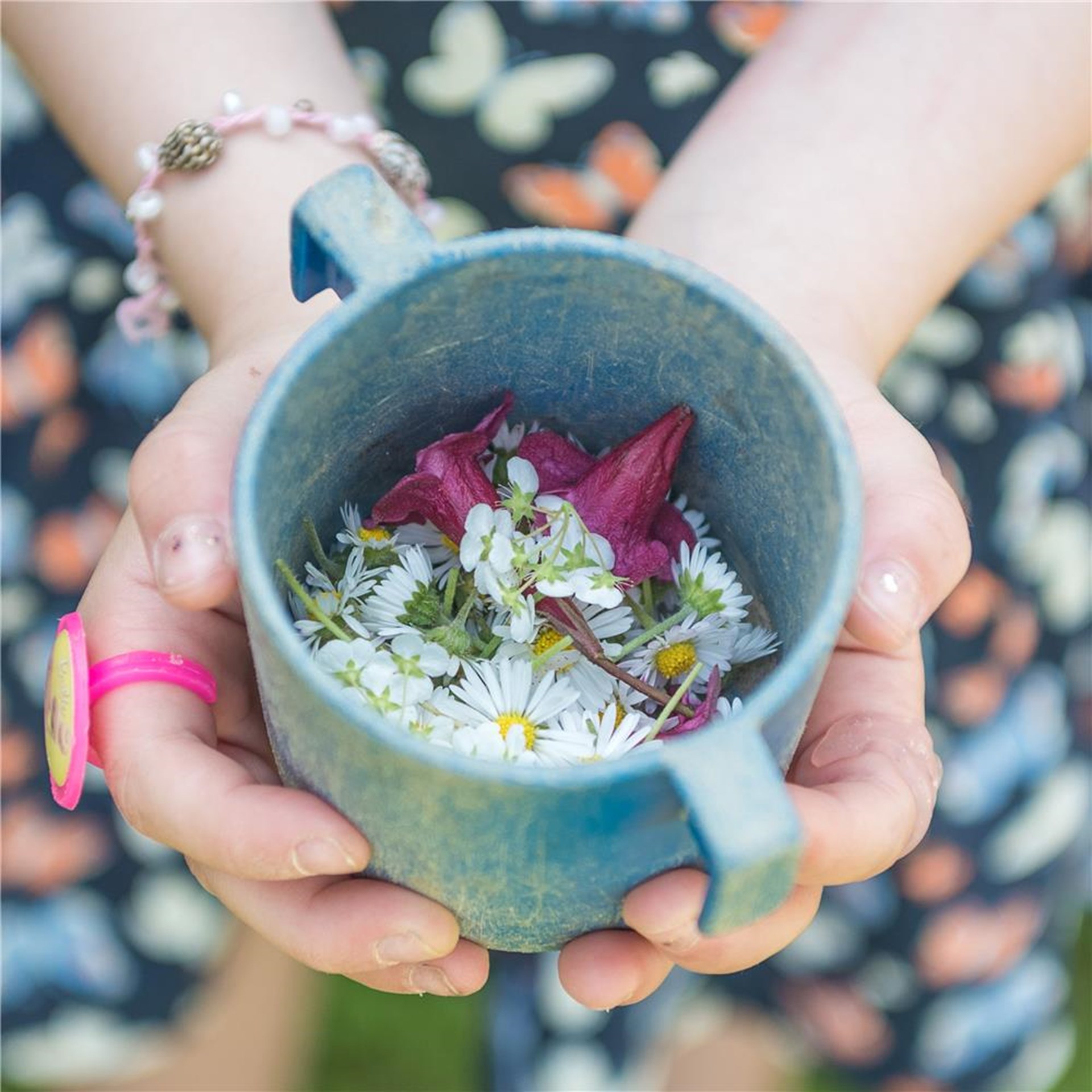 Es sind Kinderhände abgebildet, die einen Becher gefüllt mit bunten Blumen halten.